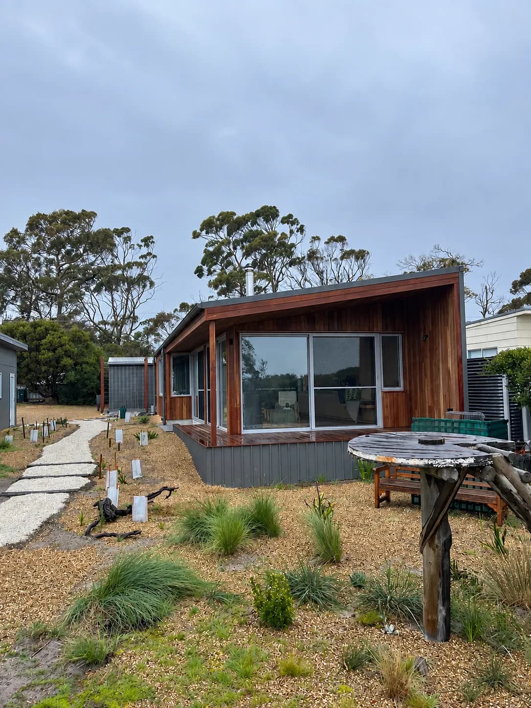 A timber clad home with a deck, standing among coastal scrub and eucalypts